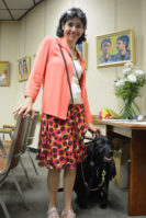 Suzanne Posner poses with her service dog by a line of portraits and a table with flowers, business cards and a sign-in paper with comments about her work. (Photo by Janelle Clausen)