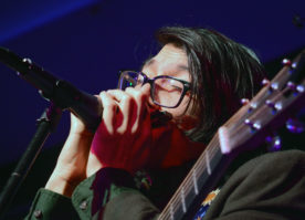 Billy Conahan, one of the vocalists and guitarists of All Types of Kinds, switches it up by playing a harmonica. (Photo by Janelle Clausen)