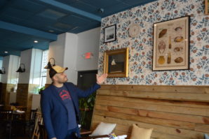 Villalona gestures to works on the wall of Element Seafood, some of which he said are heirlooms of Nellie Wu's family, which initially helped start the venture. (Photo by Janelle Clausen)