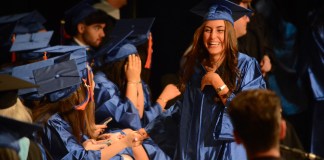 A student reaches out to a line of fellow graduates as she walks down stage to receive her diploma. (Photo by Janelle Clausen)