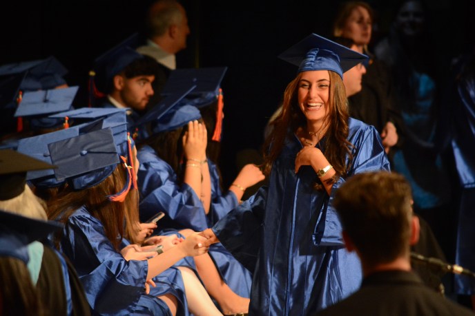 A student reaches out to a line of fellow graduates as she walks down stage to receive her diploma. (Photo by Janelle Clausen)