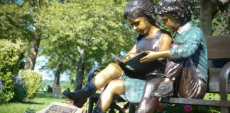 Two bronze children sit perched on a bench underneath a magnolia tree and adjacent to a memorial plaque for Ruth Tamarin. (Photo by Janelle Clausen)