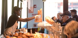 An employee of Marie Blachére passes along a baguette to one of the many customers on line ordering French pastries. (Photo by Janelle Clausen)