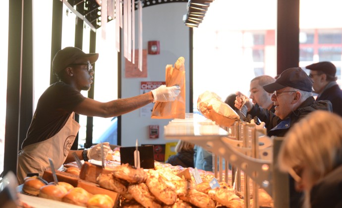 An employee of Marie Blachére passes along a baguette to one of the many customers on line ordering French pastries. (Photo by Janelle Clausen)